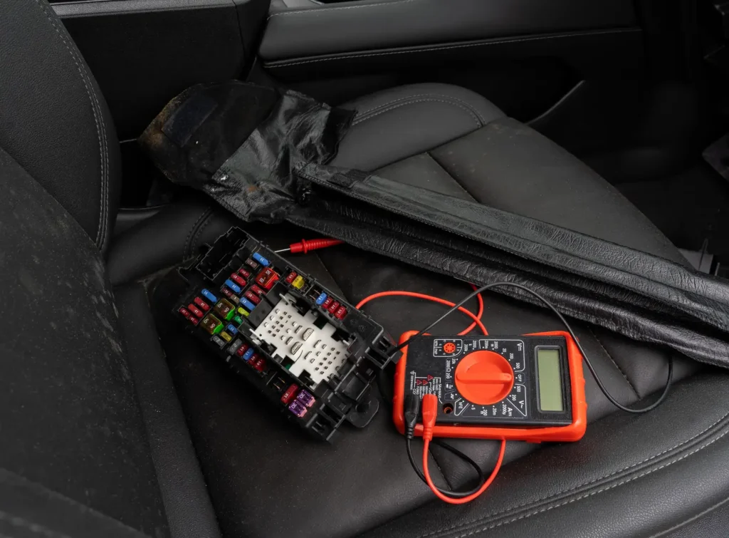 Auto drošinātāju bloks un multimetrs uz sēdekļa elektronikas diagnostikas laikā