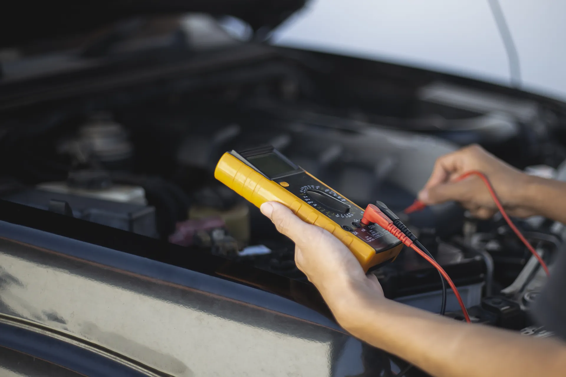 Meistars ar multimetru mēra elektrisko ķēdi auto dzinēja nodalījumā
